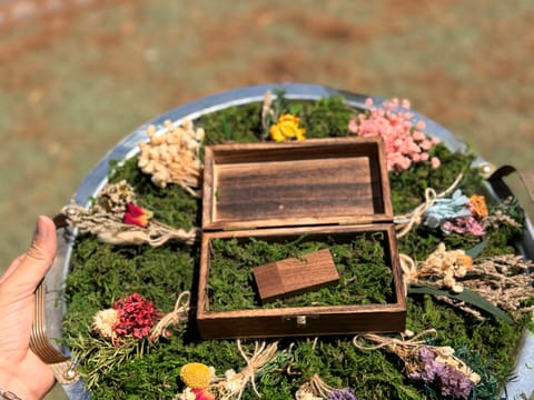 An open wooden keepsake box with a walnut USB drive resting on moss inside, surrounded by small bunches of dried flowers.